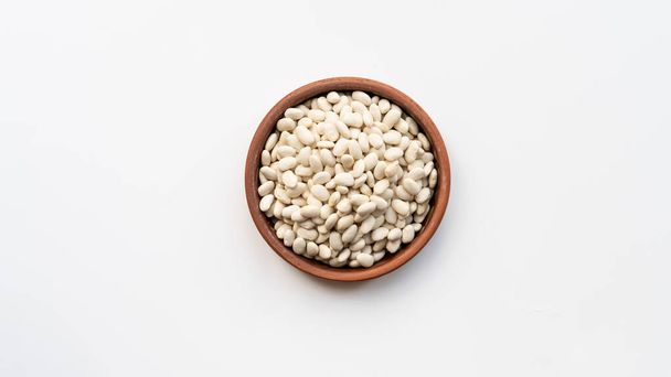 white beans in brown ceramic bowl. bowl of white kidney beans. navy, cannellini bean on white background isolated top view photo - Foto, Imagen