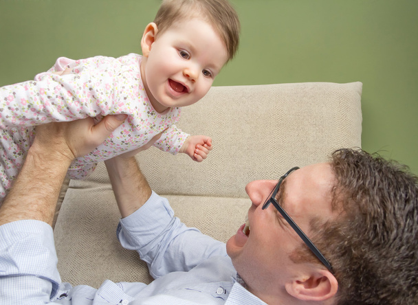 Cute baby playing with her happy father in a sofa - Фото, изображение