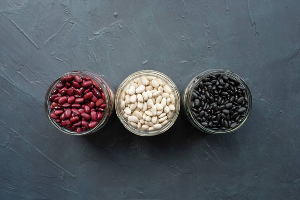 黒豆と赤豆と白豆のグラス瓶。ネイビー、カネリーニ、黒灰色の背景に白い腎臓豆。豆瓶の上から見た直線の形写真 - 写真・画像