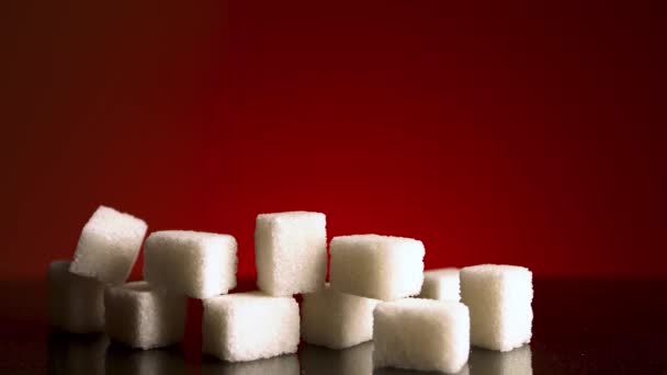 Close up de pilha crescente de cubos de açúcar isolado no fundo vermelho escuro. Imagens de stock. Parar o efeito de movimento, conceito do aumento do consumo de açúcar. - Filmagem, Vídeo