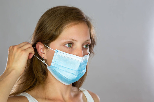 Female model in white shirt attaching surgical face mask on light background - Foto, immagini