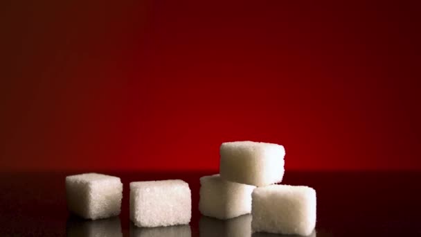 Light shines on stack of sugar cubes that lying on dark table surface isolated on red background. Stock footage. Close up of white sugar, concept of food and cooking.  - Footage, Video