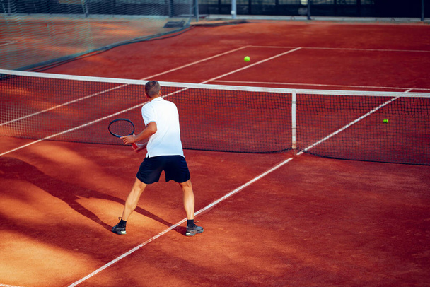 Back view of a man playing tennis on tennis court - Foto, Bild