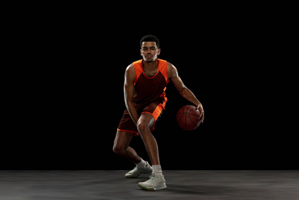Young african basketball player training on black studio background. - 写真・画像