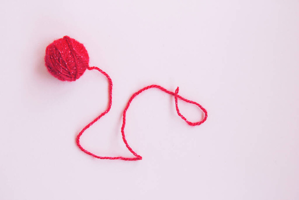 Una bola roja de hilo de lana con hilo largo y retorcido sobre un fondo rosa con espacio para copiar - Foto, imagen