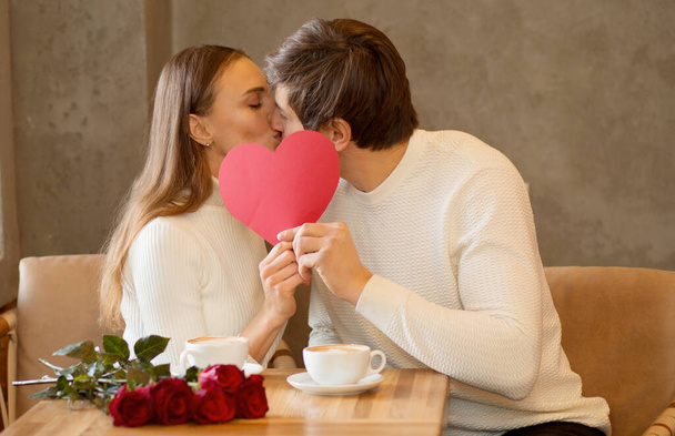 Young couple sitting in caffe with coffee holding paper heart  - Photo, Image