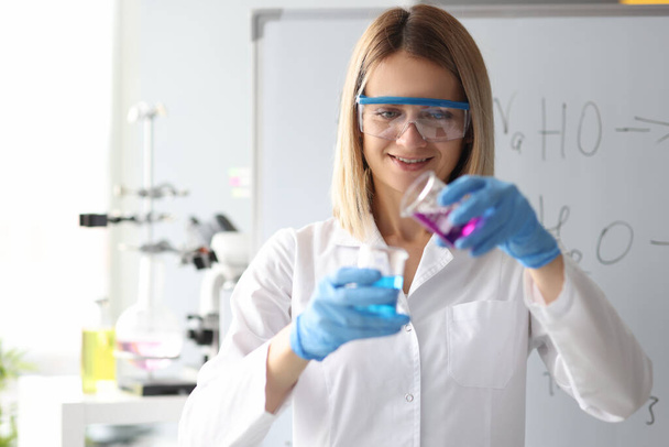Femme scientifique dans des lunettes de sécurité versant une solution chimique du flacon en laboratoire - Photo, image