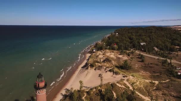 Küçük Samur Deniz Feneri 'nden uçarak uzaklaşan güzel hava manzarası Michigan Gölü kıyıları boyunca ağaçlarla kaplı kumulların ve bitki örtülerinin arasında dalgalar içeri girerken açık mavi gökyüzü.. - Video, Çekim