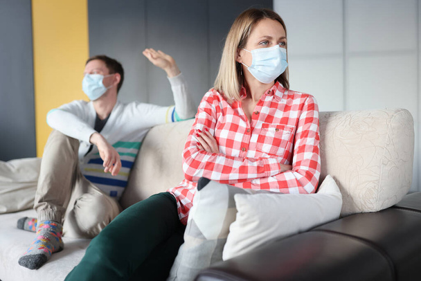 Men and women in protective medical masks siting on couch and swearing - Foto, Imagen