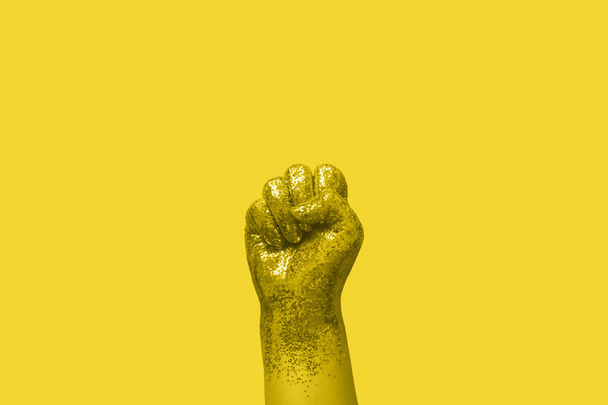 feminismo activismo concepto mujer puño cubierto de brillo de oro sobre fondo amarillo - Foto, imagen