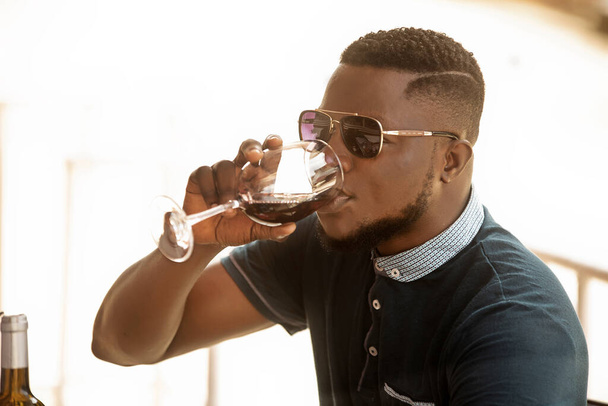 pohledný mladý muž nosí sluneční brýle pití červené víno venku - Fotografie, Obrázek