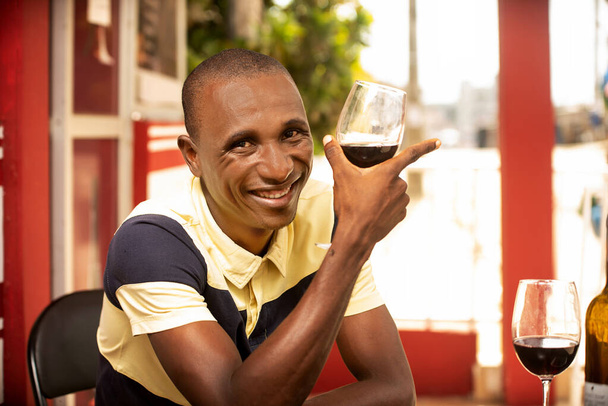красивий молодий чоловік тримає келих червоного вина і дивиться на камеру, посміхаючись
 - Фото, зображення