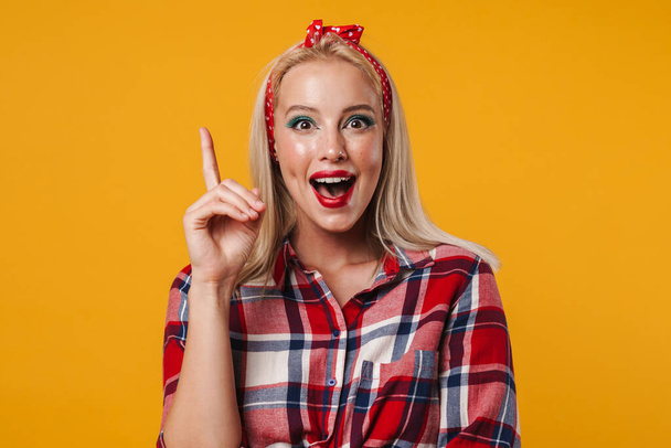 Image of excited blonde pinup girl pointing finger upward isolated over yellow background - Fotografie, Obrázek