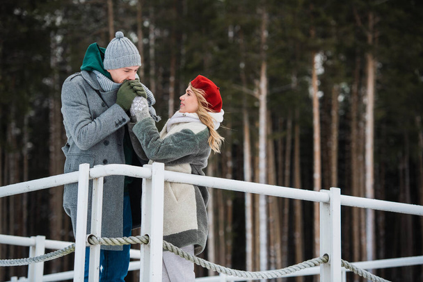 A young husband and wife stand on the bridge in an embrace against the background of a winter forest - Photo, Image
