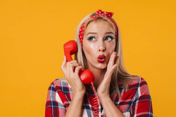 Image of surprised beautiful pinup girl posing with handset isolated over yellow background - Fotoğraf, Görsel