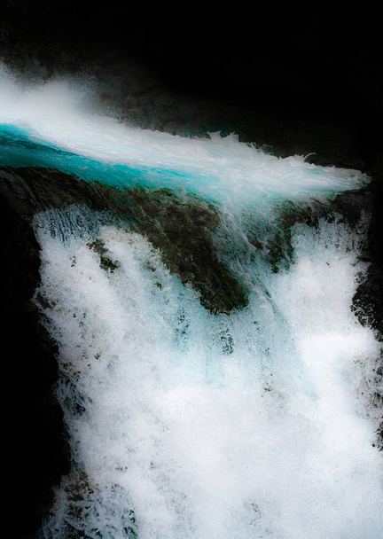 Waterfall dropping of a cliffs edge with turquoise water and white foam. Close up isolated on black. . High quality photo - Photo, Image