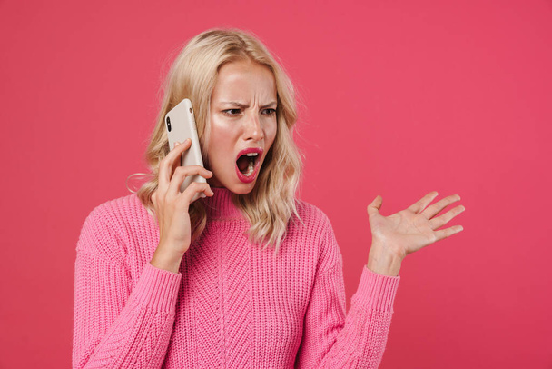 Image of furious blonde girl screaming while talking on mobile phone isolated over pink background - Фото, зображення
