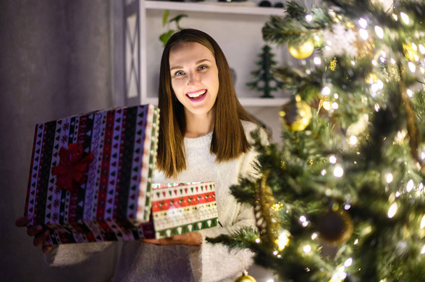 A young woman with a gift box near Christmas tree - Foto, Imagen