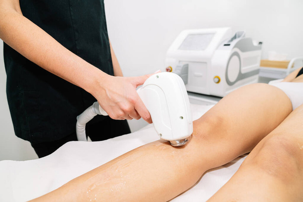 Close-up of a diode in the hand of an Aesthetician giving laser hair removal treatment to a woman on her thigh - Zdjęcie, obraz