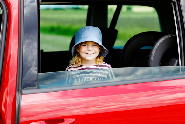 Чарівна дівчинка, яка сидить на автокріслі і дивиться з вікна на природу і трафік. Маленька дитина їде на машині. Безпека дітей на дорозі. Сімейна поїздка та відпустка влітку
 - Фото, зображення