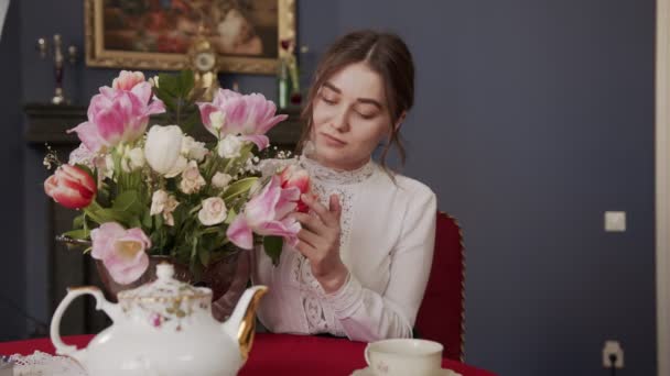 bella ragazza seduta in una stanza con un interno vintage e gode l'aroma di tulipani profumati - Filmati, video