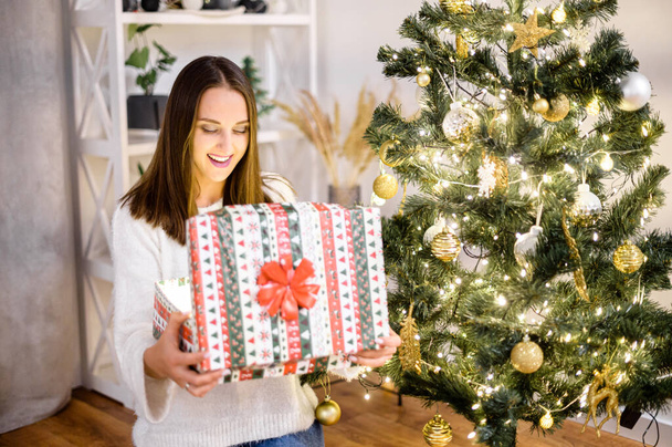 A young woman with a gift box near Christmas tree - Фото, изображение