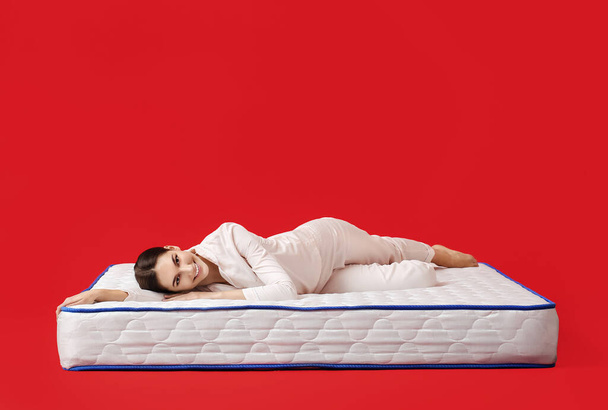 Young woman lying on mattress against color background - Photo, Image