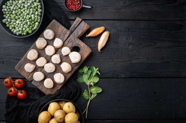 Meeresdelikatessen, Jakobsmuscheln mit Kartoffeln, grünen Erbsen und Minze, Draufsicht, auf schwarzem Holzhintergrund mit Kopierraum - Foto, Bild