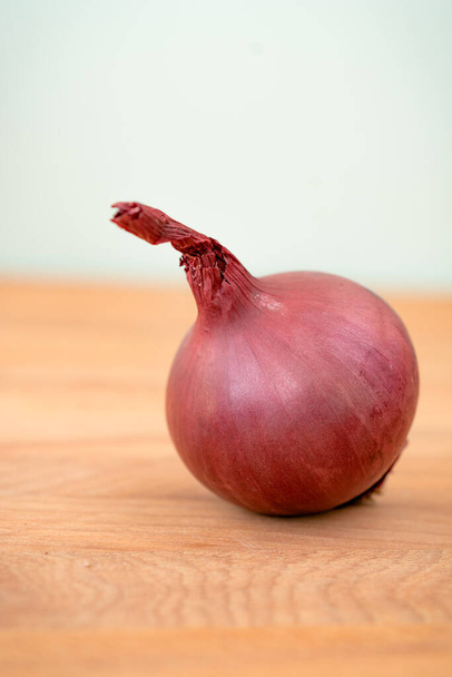 One red onion on a wooden table. Organic, fresh red onion. A healthy vegetable. Ingredients for cooking. Close-up from the side. Barrier to viruses. vertical photo - Photo, Image