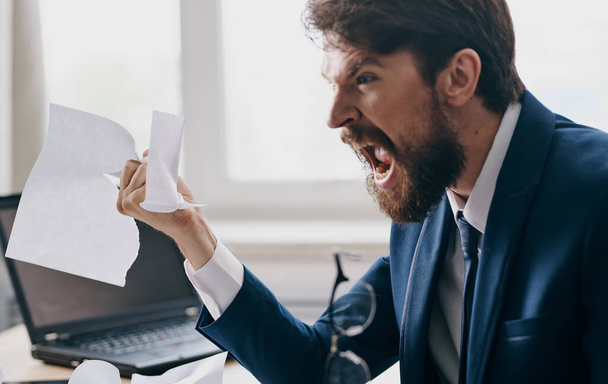 Homem de negócios agressivo em um terno com folhas brancas de papel em suas mãos no escritório perto da janela - Foto, Imagem