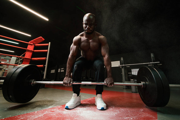 muscular African American man lifts a heavy barbell for powerlifting. Heavyweight in the smoke of talcum powder or magnesia - Φωτογραφία, εικόνα