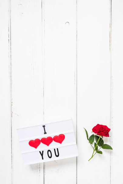 Valentine's day, love, romance concept. Fresh red rose flower and text I LOVE YOU on lightbox on white wooden background. Greeting card. Flat lay, top view, copy space. - Foto, immagini
