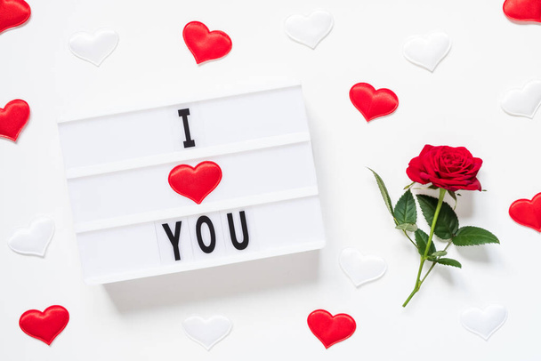 Valentine's day, love, romantic concept. Fresh red rose flower with ribbon and text I love you on lightbox on white background. Greeting card. Flat lay, top view. - 写真・画像