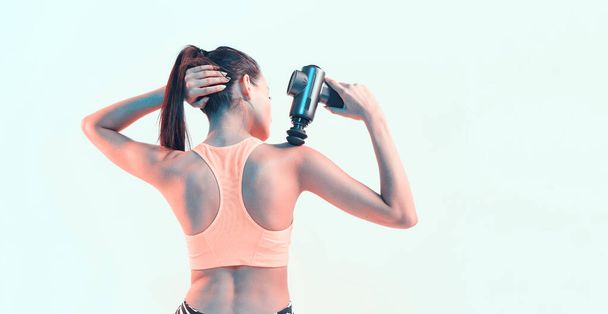 Percussion massager, sports young brunette female massaging shoulder in neon studio light, therapy for joint pain relief - 写真・画像