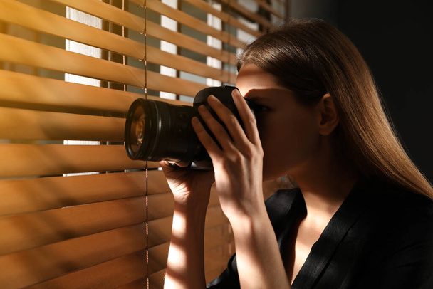 Private detective with camera spying near window indoors - Zdjęcie, obraz