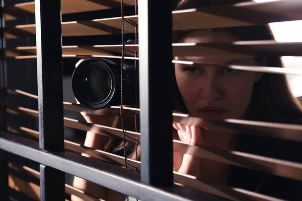 Private detective with camera spying near window indoors, closeup - 写真・画像