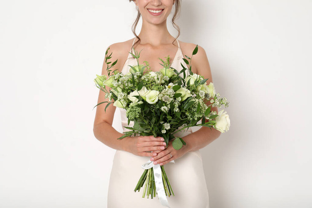 Young bride wearing wedding dress with beautiful bouquet on light background, closeup - Photo, image