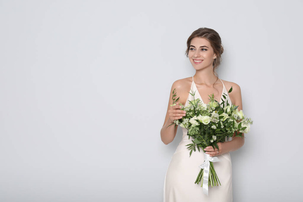 Young bride wearing wedding dress with beautiful bouquet on light grey background. Space for text - Фото, изображение