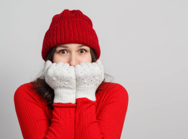 a woman in a red sweater, knitted hat warms her face with mittens. on a white background. - Valokuva, kuva