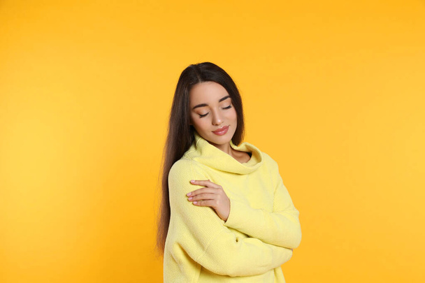 Beautiful young woman wearing warm sweater on yellow background - 写真・画像