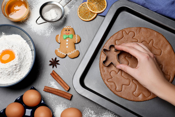 Woman making Christmas gingerbread man cookies at grey table, closeup - Photo, Image