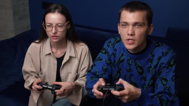  молодые люди играют в видеоигры на консоли, сидя на диване перед телевизором. Тысячелетняя пара проводит время вместе дома. - Кадры, видео