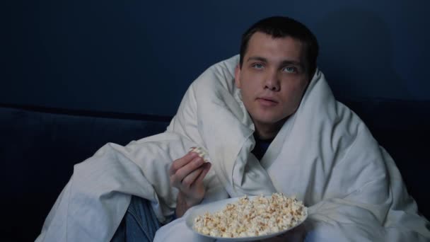 Portret verveelde blanke man zit op de bank thuis met deken gooien popcorn en vangen met zijn mond, zelf isolatie tijd thuis concept - Video