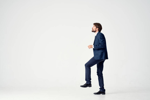 homem de negócios em um terno azul fica em uma perna em uma vista lateral de fundo leve - Foto, Imagem