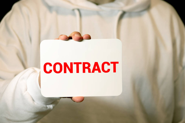 Hands holding a card with the inscription: first contract - Photo, Image