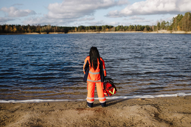 Paramédico femenino posando cerca del lago azul en un día soleado - Foto, imagen
