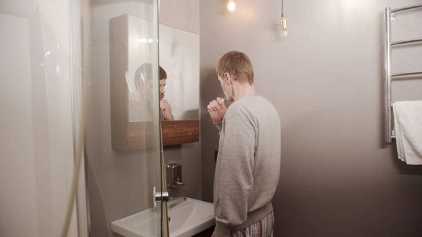 In the hotel bathroom in the early morning a man brushes his teeth after waking up - Foto, afbeelding