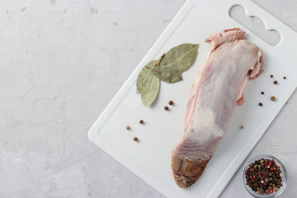 Raw pork tongue, peppers mix and bay leaf on a plastic white board. View from above. Space for text - Photo, Image