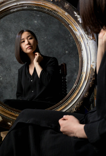 Beautiful young asian woman looking on her reflection at the mirror - Valokuva, kuva
