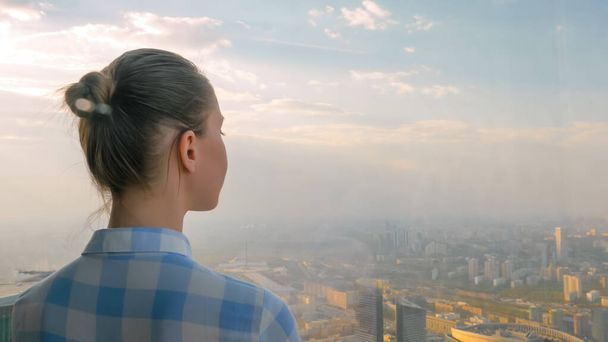 Женщина, смотрящая на городской пейзаж через окно небоскреба - вид сзади - Фото, изображение